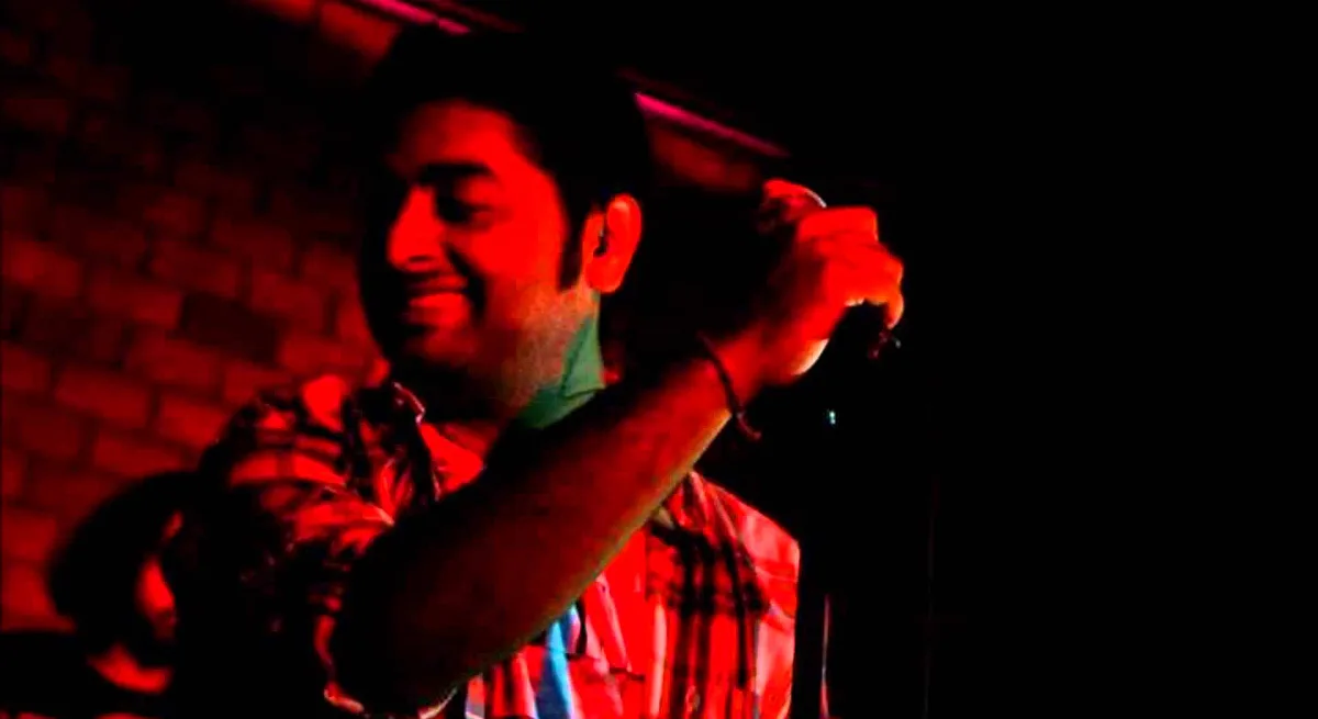 Arijit Singh singing live under red concert lights, microphone in hand