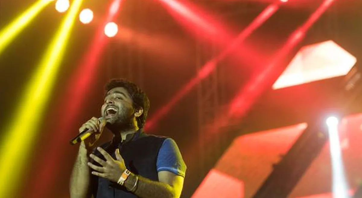 Arijit Singh performing live at MMRDA Grounds, Mumbai — stage lights sweeping red and gold over the crowd