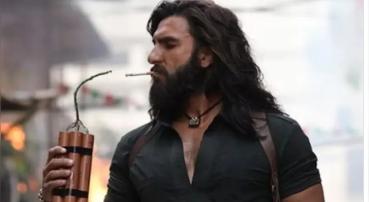 Ranveer Singh as Jaskirat Singh Rangi in Dhurandhar — blast-scarred street, smoke and fire behind him, detonator in hand