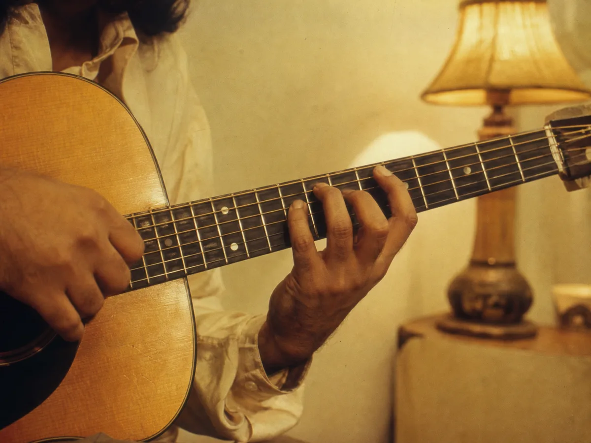 Hands on an acoustic guitar fretboard in a warm studio