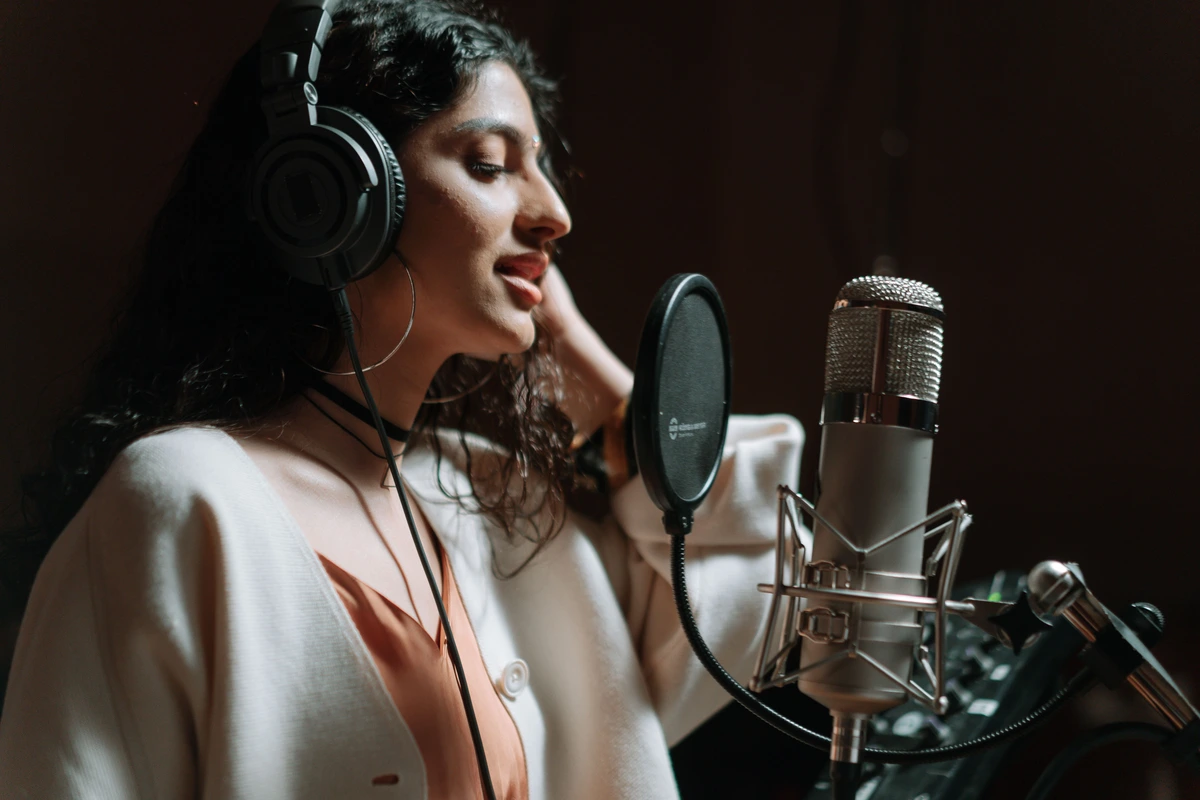 A singer with headphones recording vocals at a studio condenser microphone fitted with a pop filter